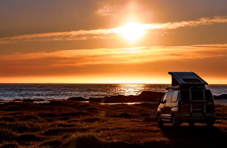 Volkswagen Multivan mit geöffnetem Dach beim Camping am Meer während des Sonnenuntergangs – Thema: VW T6 Preise und Nutzungsmöglichkeiten
